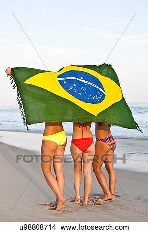 Picture - Rear view of three young women on beach in bikinis with Brazilian Flag. Fotosearch