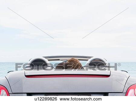 Rear view of young couple sitting in convertible sports car View Large Photo Image Stock Photograph - Rear view of young couple sitting in convertible sports car. Fotosearch