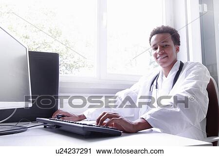 Stock Image - Scientist wearing lab coat working on computer. Fotosearch