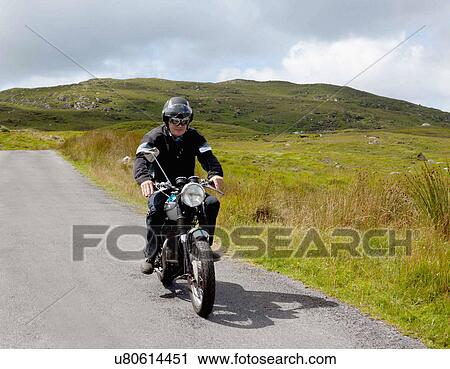 Stock Image - Senior male motorcyclist riding on rural road. Fotosearch