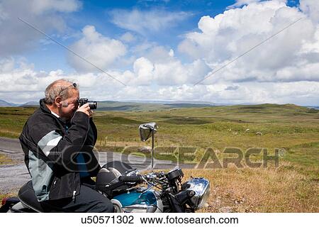 Senior male motorcyclist taking a photograph of scene View Large Photo Image Stock Image - Senior male motorcyclist taking a photograph of scene. Fotosearch