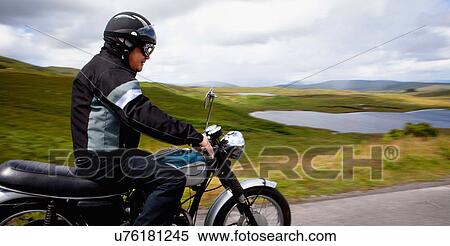 Stock Photography - Senior male riding motorbike through rural landscape. Fotosearch