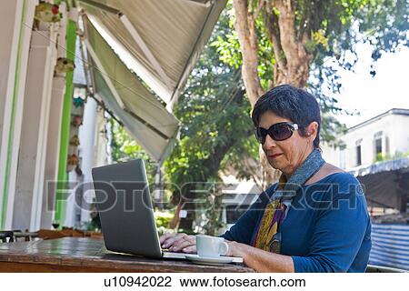 Stock Image - Senior woman using laptop at cafe. Fotosearch