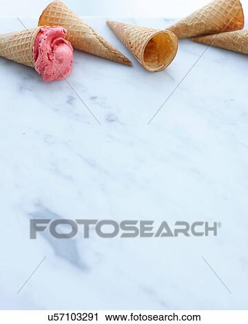 Stock Image - Still life of empty cones and one with scoop of strawberry ice cream. Fotosearch