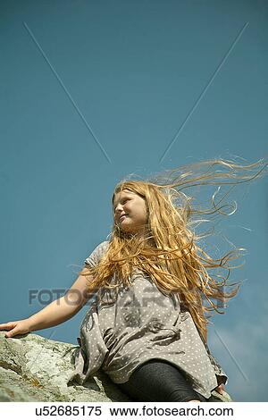 Stock Photography - Teenage girl with long red hair sitting on rocks in wind. Fotosearch