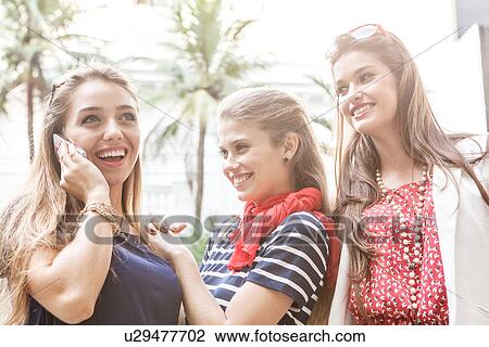 Stock Image - Three female friends using cellphone. Fotosearch