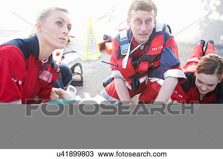 Stock Image - Three paramedics tending patient lying on road. Fotosearch