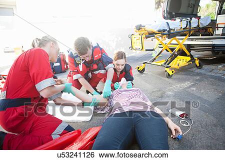 Three paramedics tending patient on road View Large Photo Image Stock Photograph - Three paramedics tending patient on road. Fotosearch
