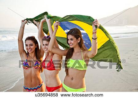 Stock Photo - Three young women on beach with Brazilian Flag. Fotosearch