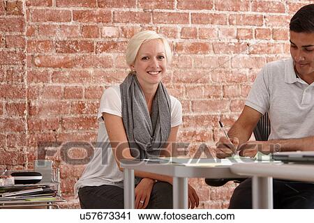 Stock Image - Two colleagues at desk, man making notes. Fotosearch