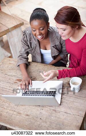 Stock Image - Two female friends looking at laptop in street cafe. Fotosearch