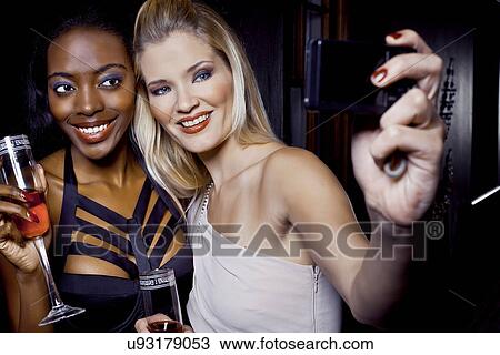 Stock Image - Two female friends making self portrait in nightclub. Fotosearch