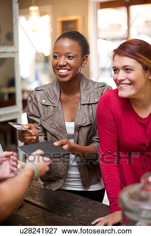 Stock Photo - Two female friends paying bill in cafe. Fotosearch