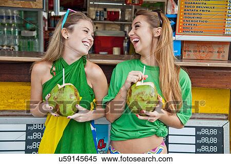 Stock Photography - Two happy young women with coconut drinks, Ipanema Beach, Rio, Brazil. Fotosearch