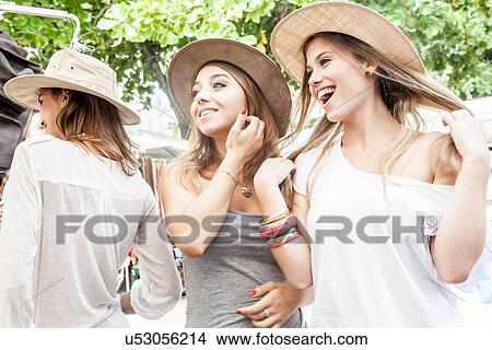 Two young women trying on hats in market View Large Photo Image Picture - Two young women trying on hats in market. Fotosearch