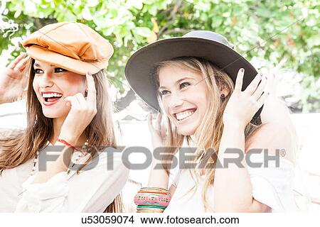Two young women trying on hats in market View Large Photo Image Picture - Two young women trying on hats in market. Fotosearch