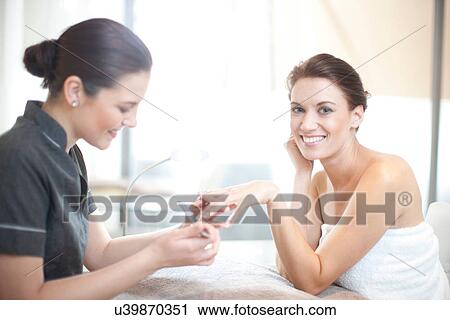Stock Image - Woman having her nails filed in spa treatment room. Fotosearch