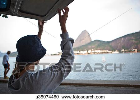Stock Image - Woman lifting campervan door, Rio de Janeiro, Brazil. Fotosearch