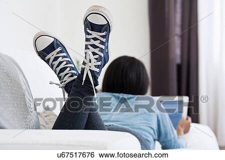 Woman lying on sofa using digital tablet View Large Photo Image Stock Photograph - Woman lying on sofa using digital tablet. Fotosearch