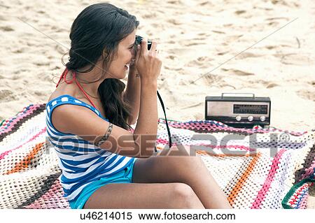 Stock Photography - Woman on blanket on beach using camera. Fotosearch
