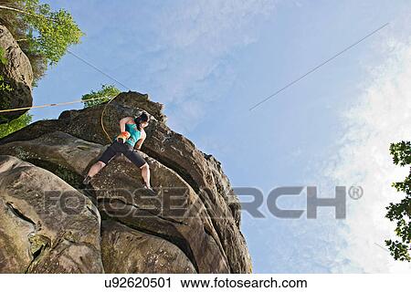 Stock Image - Woman on top rope climbing sandstone butte. Fotosearch