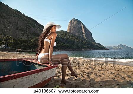 Stock Photo - Woman sitting on boat on beach, Rio de Janeiro, Brazil. Fotosearch