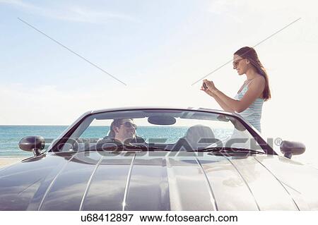 Woman taking photograph of man in sports car View Large Photo Image Stock Photo - Woman taking photograph of man in sports car. Fotosearch