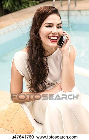 Stock Image - Woman wearing white dress on cell phone, laughing. Fotosearch