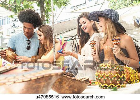 Stock Photograph - Young adults looking at souvenirs in market. Fotosearch
