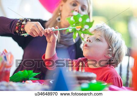 Stock Image - Young boy blowing windmill at birthday party. Fotosearch