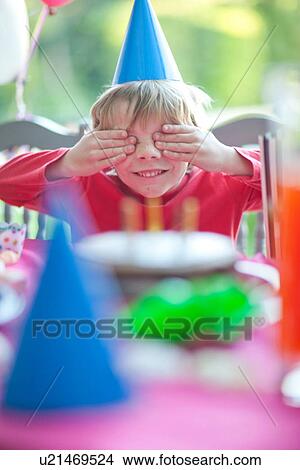 Picture - Young boy with hands over eyes at birthday party. Fotosearch