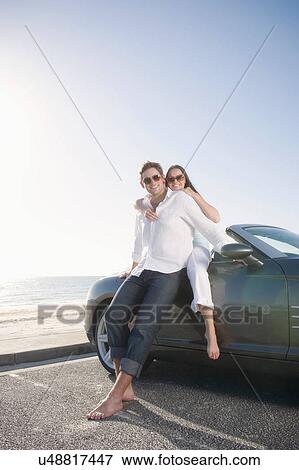 Young couple beside convertible sports car View Large Photo Image Stock Photo - Young couple beside convertible sports car. Fotosearch