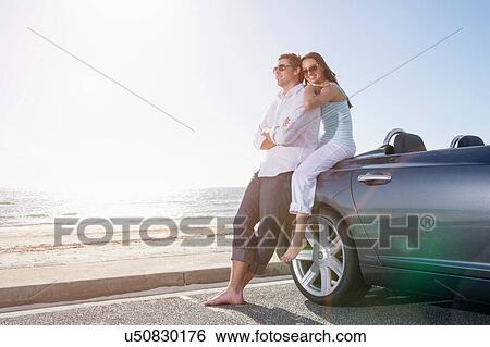Stock Photograph - Young couple beside convertible sports car. Fotosearch