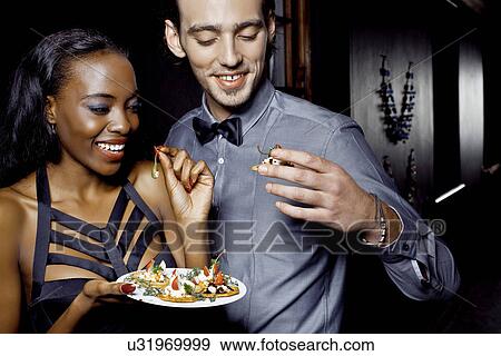 Stock Photo - Young couple eating snacks in nightclub. Fotosearch