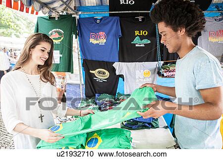 Stock Image - Young couple looking at t-shirts in market. Fotosearch