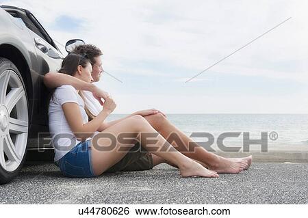 Stock Photograph - Young couple sitting beside convertible sports car. Fotosearch