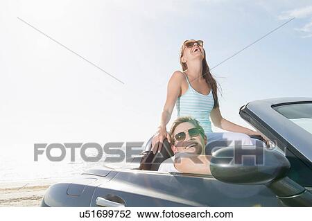 Stock Image - Young couple sitting in convertible sports car. Fotosearch