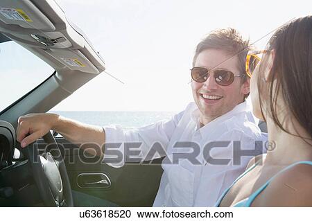 Stock Image - Young couple sitting in convertible sports car. Fotosearch