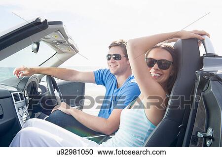 Stock Image - Young couple sitting in convertible sports car. Fotosearch