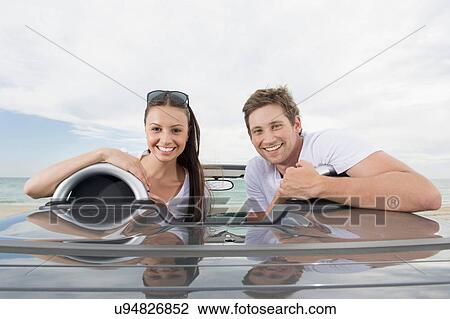 Stock Image - Young couple sitting in convertible sports car. Fotosearch
