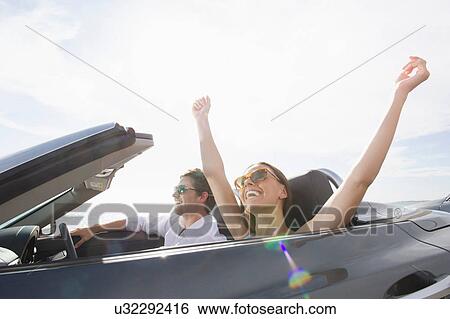 Young couple sitting in convertible sports car, arms raised View Large Photo Image Stock Photograph - Young couple sitting in convertible sports car, arms raised. Fotosearch