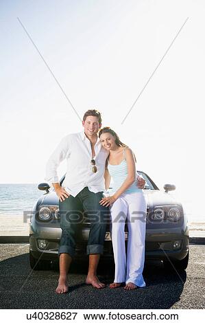 Young couple sitting on bonnet of sports car View Large Photo Image Stock Photo - Young couple sitting on bonnet of sports car. Fotosearch