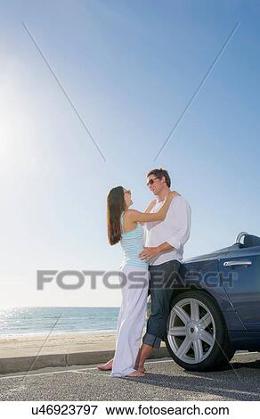 Young couple standing beside convertible sports car View Large Photo Image Stock Photo - Young couple standing beside convertible sports car. Fotosearch