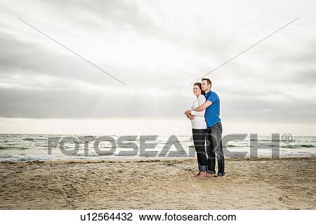 Stock Image - Young couple standing hugging on beach. Fotosearch