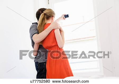 Stock Image - Young couple taking photograph from window. Fotosearch
