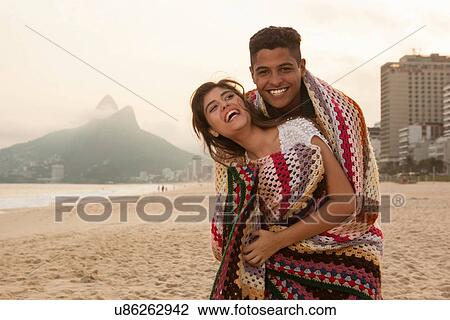Stock Image - Young couple wrapped in blanket, Ipanema Beach, Rio de Janeiro, Brazil. Fotosearch