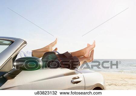 Stock Image - Young couple's feet out of top of convertible sports car. Fotosearch