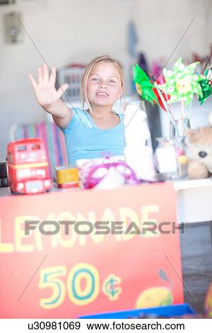Stock Photo - Young girl behind stall with her hand up. Fotosearch