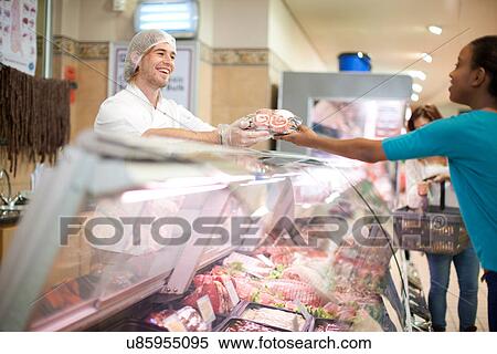 Stock Photography - Young male sales assistant serving customer at counter. Fotosearch