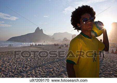 Stock Image - Young man at the beach with football, Ipanema Beach, Rio, Brazil. Fotosearch